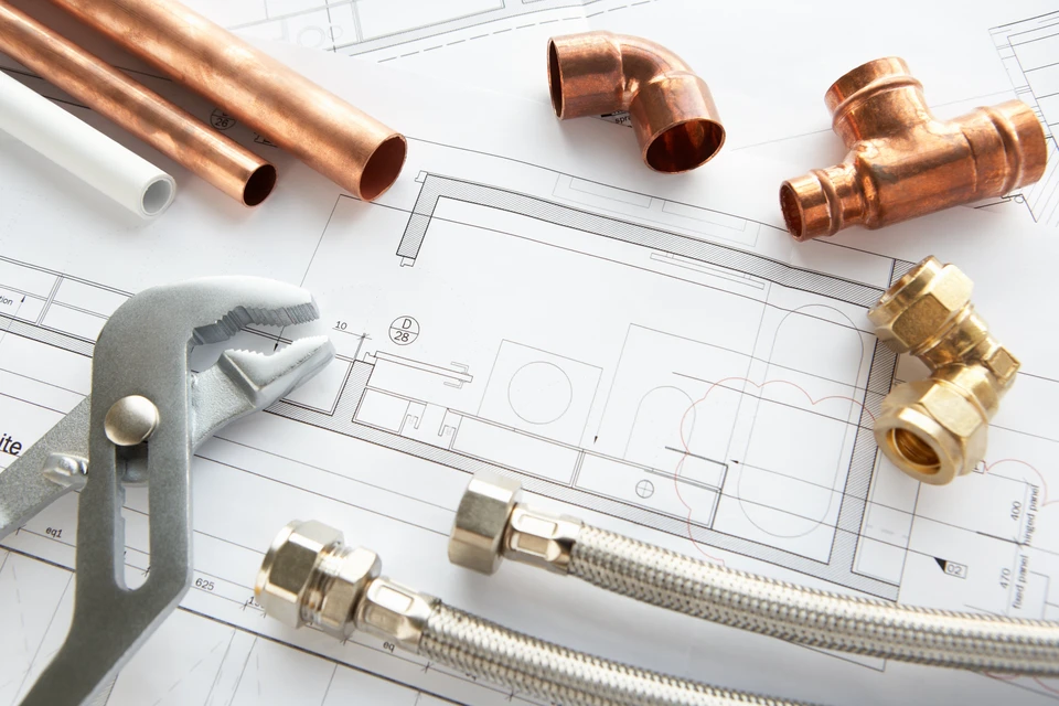 Plans techniques d'architecture sur table avec outils de plomberie professionnels disposés autour