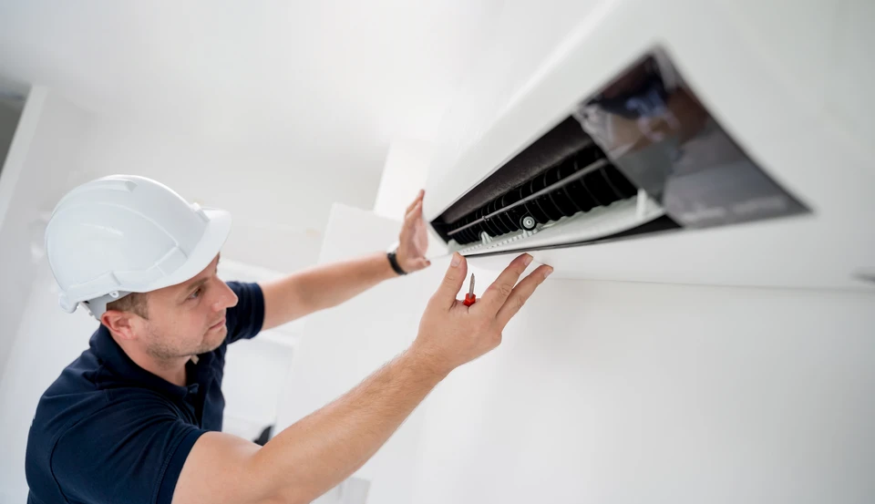 Technicien en casque blanc effectuant la maintenance d'un climatiseur mural split dans un intérieur résidentiel