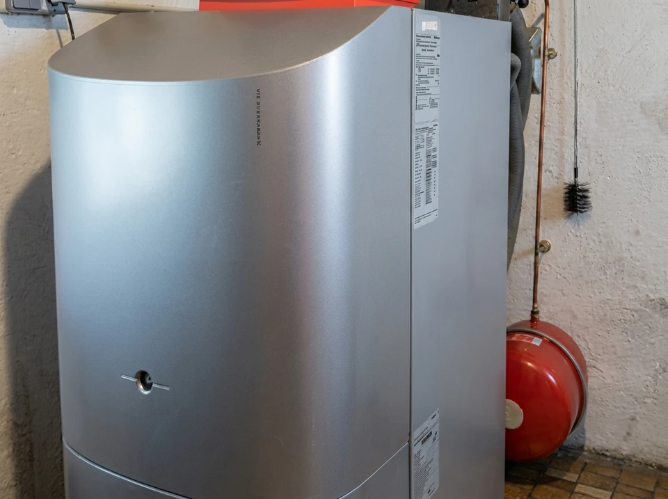 Un homme travaille sur un système de chauffage sous-pente dans un espace réduit, manipulant des connexions hydrauliques avec un outil spécialisé