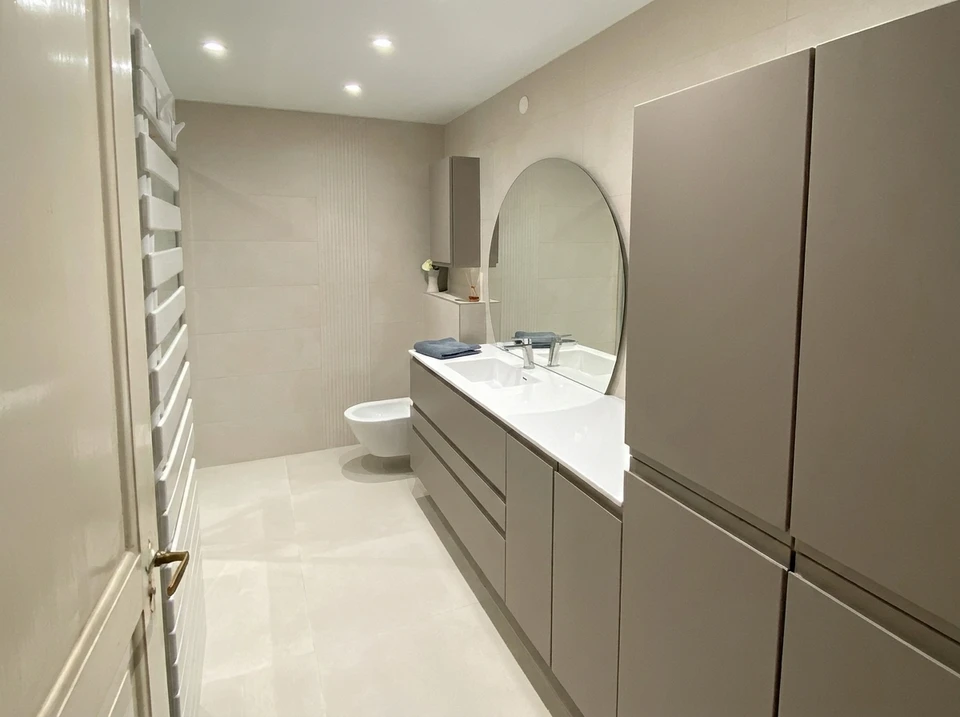 Salle de bain moderne rénovée avec baignoire encastrée, meuble-lavabo bleu clair, miroir encadré et carrelage beige